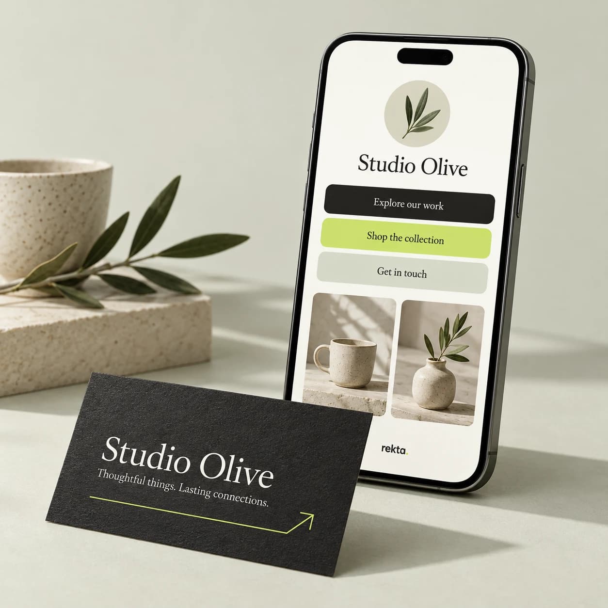 Illustrative Studio Olive Rekta Page on a phone beside its matching charcoal business card, with lime accents and ceramic product photos.